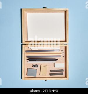 Flat lay artistic wooden box with art tools, pencils, pens and others on blue. Stock Photo