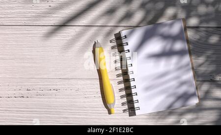 Notepad and pen on wood table, with shadow of palm leaves. Stock Photo