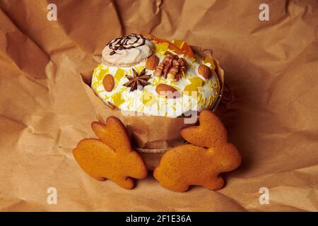Easter cake on the brown paper with gingerbread cookies. Handmade panettone decorated with liquid icing sugar almonds, walnut and meringue. Stock Photo