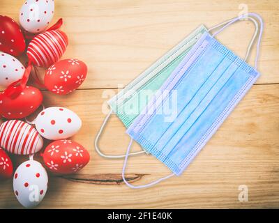 Easter holiday celebration at Coronavirus pandemic. Covid19 protective masks and Easter eggs on wooden table background, top view. Stock Photo