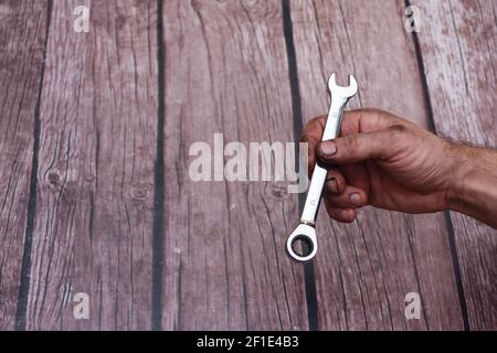 Male hand worker holding wrench, on a wooden background. With an inscription. Stock Photo