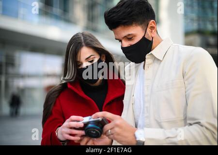 Happy tourists with covid or coronavirus masks couple whalking together in a city andtaking a look at the photos shot together Stock Photo