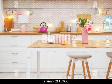 Pink vase with flowers and mugs for tea on the table in a light kitchen in the Scandinavian style. Stock Photo