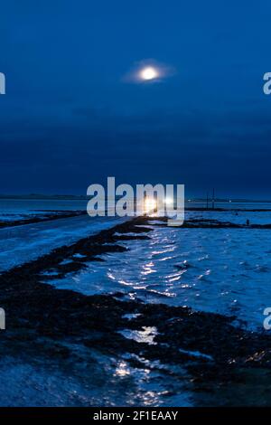 Cars crossing from Lindisfarne, Holy Island, to return to Northumberland mainland - tidal causeway in winter by moonight Stock Photo