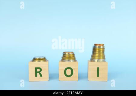 ROI or return on investment letters on wooden blocks in blue background with increasing stack of coins. Increase in business profit concept. Stock Photo