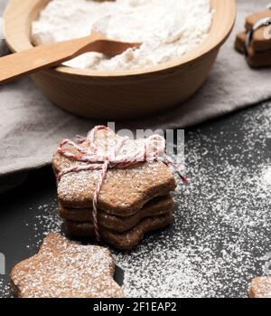 baked star-shaped gingerbread cookie sprinkled with powdered sugar on a black table and ingredients, close up Stock Photo