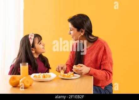 A MOTHER AND DAUGHTER LOOKING AT EACH OTHER WHILE EATING ORANGES Stock Photo