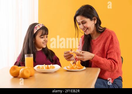 A MOTHER HAPPILY PEELING ORANGES WHILE DAUGHTER SITS BESIDE Stock Photo