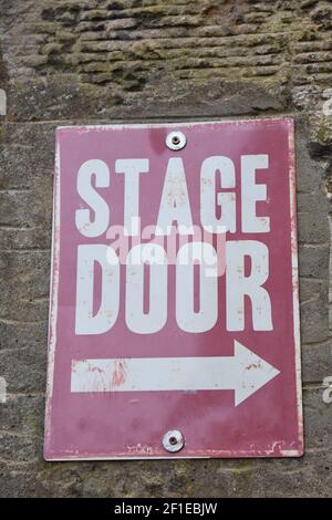 Isolated sign for Stage Door on stone wall. Sign is red and white with arrow to the right. Stock Photo