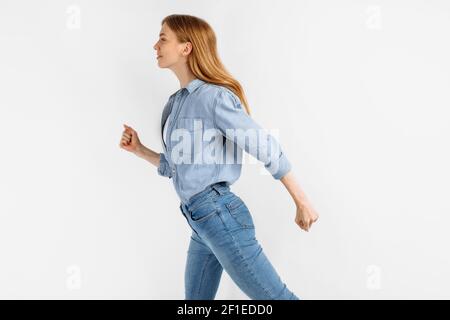 Side profile photo of cheerful beautiful young woman walking in jeans and expressing positive emotions, on white background Stock Photo