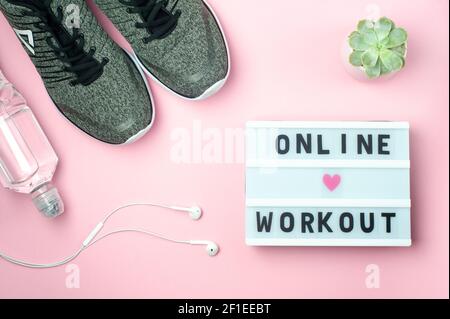 Online Workout - text on display lightbox on pink background. Flat lay - Sneakers, a bottle of water, white headphones. Sport concept. Stock Photo