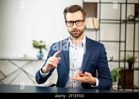 Young bearded confident entrepreneur man in business casual clothes looking at camera, presenting new product, placed hands in the position to showcase app, device, business idea. Copy space concept Stock Photo