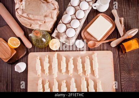 Making croissants at home. Rolls the dough into rolls for further baking. Ingredients and kitchen utencil on the background. Top view Stock Photo