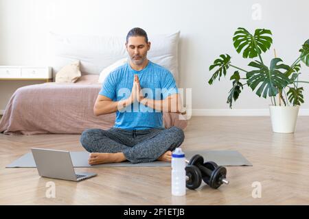 Middle aged man during online steaming. Meditation practice in front of laptop - prayer pose. Stock Photo