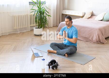 Photo of a middla aged man during online steaming. Meditation practice - prayer pose in front of laptop monitor at home. Stock Photo