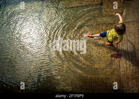 harbour slipway, child kicking surface of water, shot from above Stock Photo