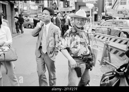 A cowboy in Tokyo: A man dressed in a cowboy costume standing in the   shinjuku district while businessman is going to work,Tokyo , Japan . Stock Photo
