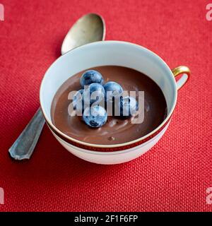 Chocolate Mousse with Fresh Blueberries in a Cup with Metal Spoon on Red Cloth Placemat Stock Photo