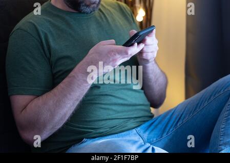 midsection on man wearing casual clothes relaxing on sofa using his smartphone Stock Photo