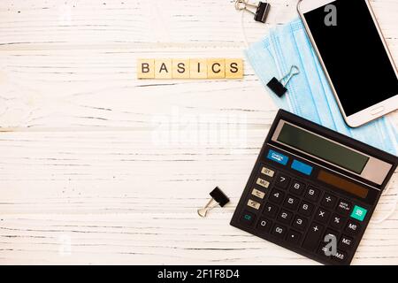 Basic income written on wood blocks with medical mask, calculator on white background. Back to basics fundamental principles concept. Stock Photo