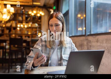 Young Caucasian business woman with blonde hair working on laptop in cafe. College student using technology , online education, freelance  Stock Photo