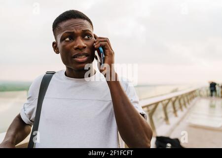 Unhappy african american guy talking on mobile phone at urban bridge outdoors Stock Photo