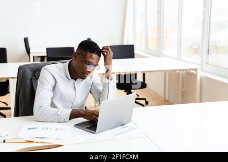 Thoughtful young african american businessman working on laptop computer Stock Photo