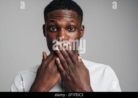 Closeup portrait of a surprised young man with hands covering closed mouth, eyes wide open in full disbelief, isolated on white background. Positive h Stock Photo