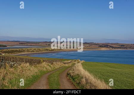 A small muddy track which forms part of the Angus Coastal Trail with a view of Lunan Bay looking North with lines of waves coming on to the Beach. Stock Photo