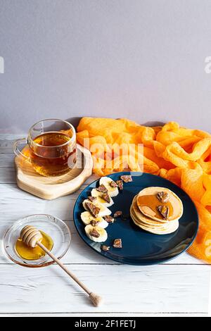 Homemade pancakes with honey, banana and chocolate. Healthy breakfast concept, copy space. A bright still life with a cup of tea, a plate of pancakes Stock Photo