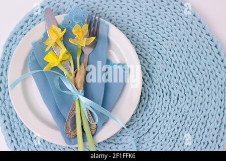 Beautiful Easter holiday table setting with cutlery. Narcissus flowers, eating utensils with bow on white plate. knitted aqua color napkin background, Stock Photo