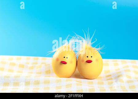 Couple of funny Easter eggs decorated as yellow chicks on a checked towel. Blue background. Stock Photo