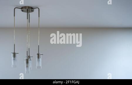 Modern metal and glass lamp with four lights hanging form the ceiling, empty space right side Stock Photo