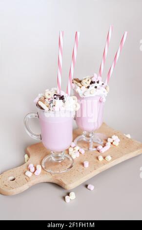 Two pink milkshakes or freakshakes with whipped cream, marshmallows, sprinkles and straws Stock Photo