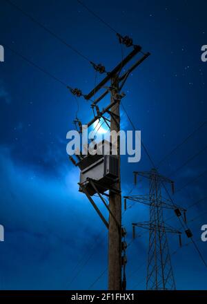 Electric power pylon cables at night blue hour moon sky. High voltage electricity substation on wooden pole tower silhouette against moody bright even Stock Photo