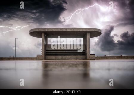 Lightning bolt strike display on sea front coast over concrete bunker shelter with dramatic storm clouds sky lit up with electricity heavy rain wet Stock Photo