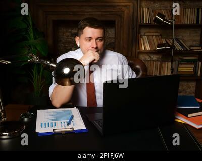 A businessman late at night communicates on the Internet and looks at a laptop. Stock Photo