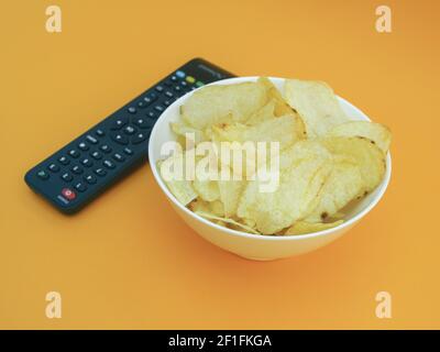 Chips in bowl and TV remote isolated on orange background, photo Stock Photo
