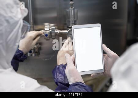 Back view close up of two workers holding tablet with blank white screen at modern chemical plant, copy space Stock Photo