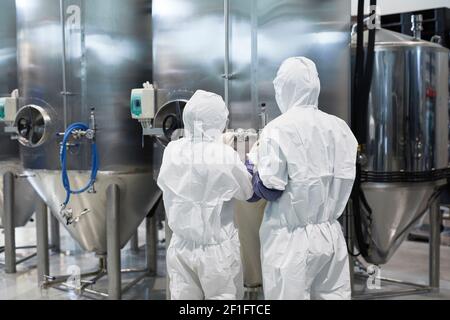Back view at two workers wearing protective suits while using machines at modern chemical plant, copy space Stock Photo