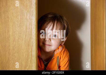 Little boy playing hide and seek in a closet. Stock Photo