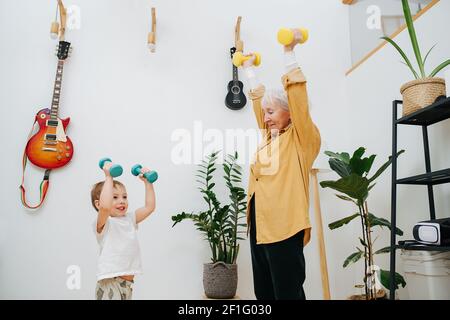 Senior woman and her young grandson together do exercises by lifting dumbbells up. High quality photo