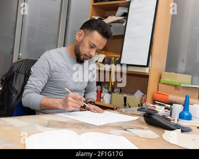 Young male immigrant working as an architect engineer designer. Doing planning work on a busy desk in the office. Stock Photo