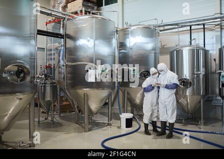 Wide angle view at two workers wearing protective suits while using digital tablet at modern chemical factory, copy space Stock Photo