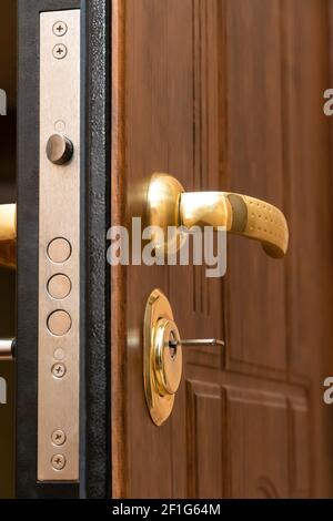 Close-up of the golden handle, the lock with the key of the beautiful brown front door. Vertical photo Stock Photo