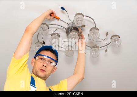 Electrician with glasses screws a chandelier to the ceiling in close-up and looks at the camera Stock Photo
