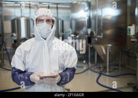 Waist up portrait of male worker wearing protective suit and looking at camera while using digital tablet at chemical factory, copy space Stock Photo