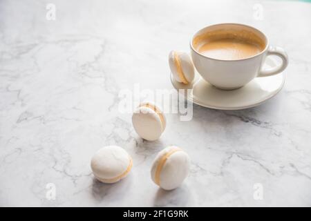 Coffee and French macaroons on marble background.Cup of aromatic coffee cappuccino with white cookies and sprinkled grains of natural roasted coffee Stock Photo