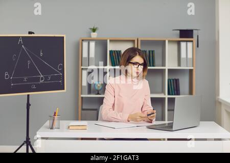 Teacher with glasses sits in front of a laptop and conducts an online math lesson via video chat. Stock Photo