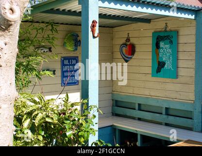 Garden seating area with wall decor including mermaids, fish, heart and  'I Do Love To Be Besides the Seaside Poster' Acuba japonica nearby. Stock Photo